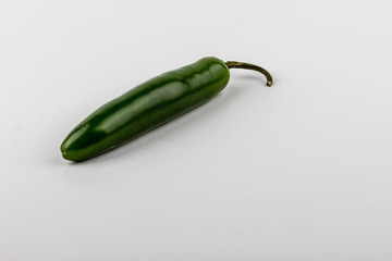 One spicy Serrano chili pepper lay on a white table against a white background. Peppers are great ingredients for cooking Latin food.