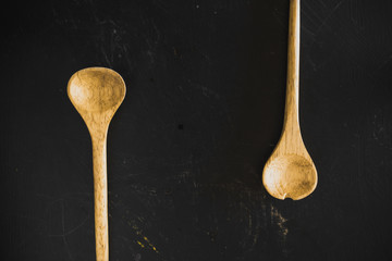 Top view of two wooden kitchen spoons in a black wooden cooking table