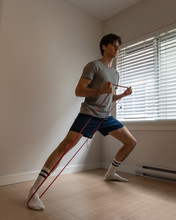 A Young Male Guy Using An Elastic Bands To Do Some Workout At Home.