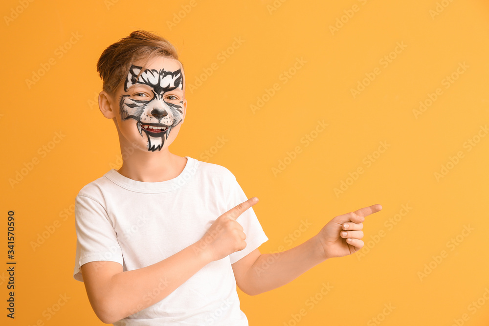 Funny little boy with face painting pointing at something on color background