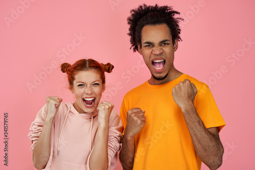 Successful mixed race team of coworkers clench fists, celebrate victory, exclaim positively, look confident, have cheerful faces, isolated on pink background. We can do it. People, success and triumph