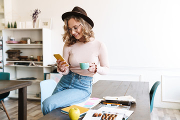 Canvas Print - Image of woman using cellphone and drinking coffee while sitting