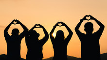 Group Of People With Raised Arms And Make Hand To The Heart Shape Looking At Sunrise On The Mountain Background. Happiness, Success, Friendship And Community Concepts.