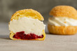 Choux pastry biscuits filled with whipped cream and raspberry jelly on grey background. Concept: bakery, french dessert. Selective focus.