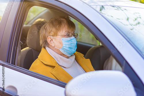 An elderly woman in a medical face mask on the passenger seat in the car. Driving to the hospital during Coronavirus pandemic concept. Road trip, travel and old people concept - happy senior couple