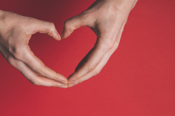 Canvas Print - Female hands creating the shape of a heart over a red background. 