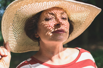 Close-up photo of senior charming brunette woman in hat blinks one eye and looking at camera