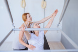 Pilates lesson on reformer, personal coach in white sportswear workout with sporty eldery beautiful grey haired woman. Rehabilitation and healty lifestyle concept.