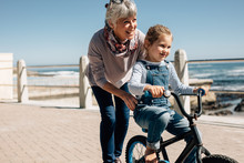 Senior Woman Helping Her Granddaughter Learn To Ride A Bicycle