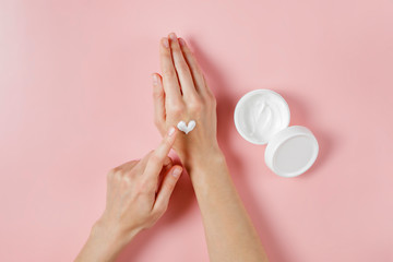 Wall Mural - Revitalizing hand cream for healing and recovery after excessive use of soap and disinfectants. Young woman applying moisturizing lotion. Copy space, close up, pink background, flat lay, top view.