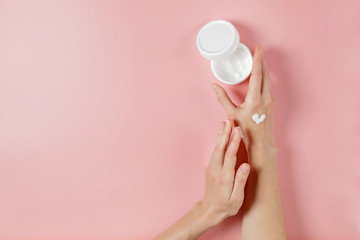 Wall Mural - Revitalizing hand cream for healing and recovery after excessive use of soap and disinfectants. Young woman applying moisturizing lotion. Copy space, close up, pink background, flat lay, top view.