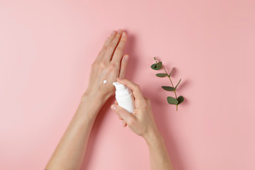 Wall Mural - Revitalizing hand cream for healing and recovery after excessive use of soap and disinfectants. Young woman applying moisturizing lotion. Copy space, close up, pink background, flat lay, top view.