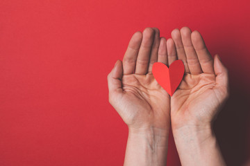 Wall Mural - Female hand holding a red paper cut out heart on a plain red background.