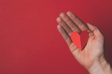 Canvas Print - Female hand holding a red paper cut out heart on a plain red background.