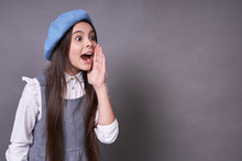 Beautiful Young Emotional Girl In A Stylish Blue Hat In A Beret On A Gray Background.