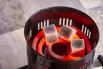 A hot stove with hookah coals stands on a light table