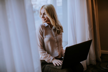 Young woman working on laptop  in living room on the window sill