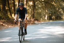 Mature Man In Sport Clothing, Protective Helmet And Sunglasses Riding Black Professional Bike With Blur Background Of Nature. Male Cyclist Enjoying Summer Days During Sport Activity.