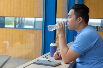 Young overweight Asian man drinking water at the coffee shop