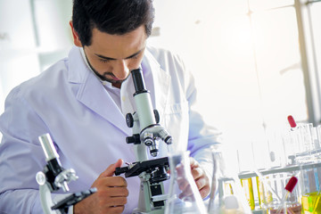 Attractive happiness scientist man lab technician assistant analyzing sample in test tube with microscope at laboratory. Medical, pharmaceutical and scientific research and development concept.