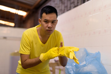 Wall Mural - Portrait of young Asian man wearing gloves while doing house chores