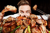 Fototapeta  - Crazy hungry man eating mix grill meat. Emotional content for restaurant promo. Cheat day. Meat lover. Lamb chops, chicken tikka, kebab, lamb, beef steak. Enjoy your food
