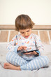 © Alex Desanshe - A little boy plays games on the phone. A child sits on a bed in pajamas with a phone