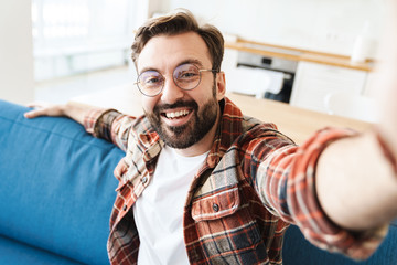 Poster - Image of happy young man smiling and taking selfie on sofa at home