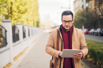 Wall Mural - Businessman walking down the street and using tablet.