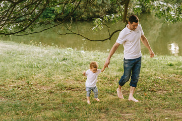 Handsome young father walking with his cute little son in sunny summer park near the lake