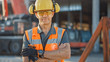 © Gorodenkoff - Portrait of Successful Builder / Worker / Contractor Wearing Hard Hat and Safety Vest Standing on a Commercial Building Construction Site, Crosses Arms Confidently. In the Background Crane Machinery