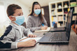 © Mediteraneo - Boy and girl studies at home, wear protective masks, and doing school homework. Distance learning online education.
