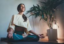 Young Happy Beautiful Woman In Cozy Cropped Sweatshirt And Leggings Practicing Yoga At Home Sitting In Lotus Pose On Yoga Mat Meditating Smiling Relaxed With Closed Eyes Mindfulness Meditation Concept