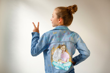 Young girl in denim jacket with a portrait drawing on the back about a teenager and her dog pet . View from the back with fingers peace victory message.