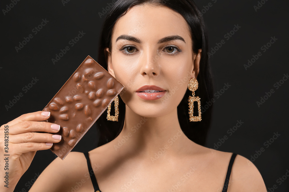 Beautiful young woman with chocolate on dark background