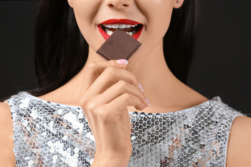 Wall Mural - Beautiful young woman with chocolate on dark background, closeup