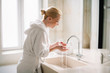 © JustLife - Beautiful woman enjoying in hotel. Young happy women in bathrobe wash her face.