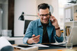 © JustLife - Businessman in office. Handsome man talking on phone at work