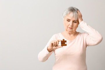 Wall Mural - Elderly woman suffering from mental disability with puzzle piece on grey background