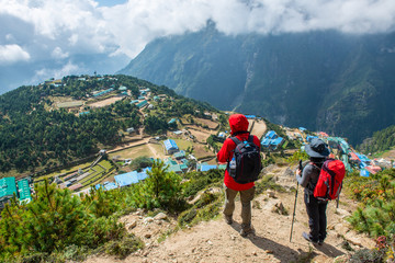 couple of tourist standing on the mountains edge and looking below to scenery view of namche bazaar 