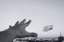 Cropped Hand Of Person Attempting To Catch Paper Against Sky