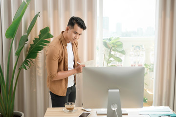 Fototapete - Asian man, aged 25-35 at the desk and smiling happily. He monitors sales on the computer screen.