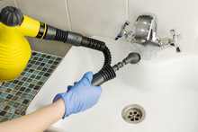 Cleaning  White Bathroom Sink And Tap With Yellow Steam Generator, Hand In Blue Glove Holds Black Hose With Brush, Which Produces Steam, Home Cleaning Concept, Mold And Calcium Control