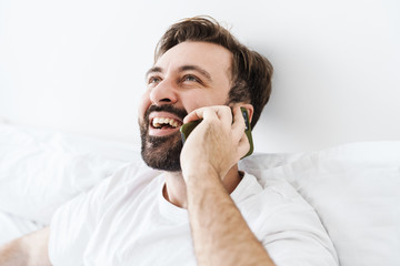 Poster - Image of caucasian man smiling and talking on cellphone in bed at home