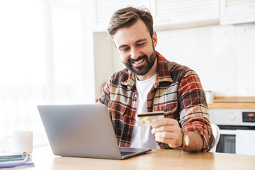 Canvas Print - Portrait of cheerful man working with laptop and holding credit card