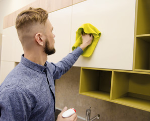 Wall Mural - Attractive bearded man cleaning the handleless cabinet doors with a yellow rag in a modern kitchen