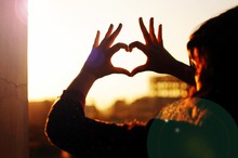 Woman Forming Heart Shape With Hands Against Clear Sky On Sunny Day