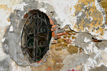 Wall Mural - Close-up of an old round window closed with a rusty iron grate on a cracked brick wall, Italy