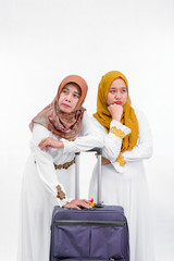 portrait of two muslim woman. mother and daughter or sister with suitcase smiling standing together waiting and look sleepy isolated over white background