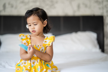 Cute little girl sitting on her bed holding alcohol gel tube. 